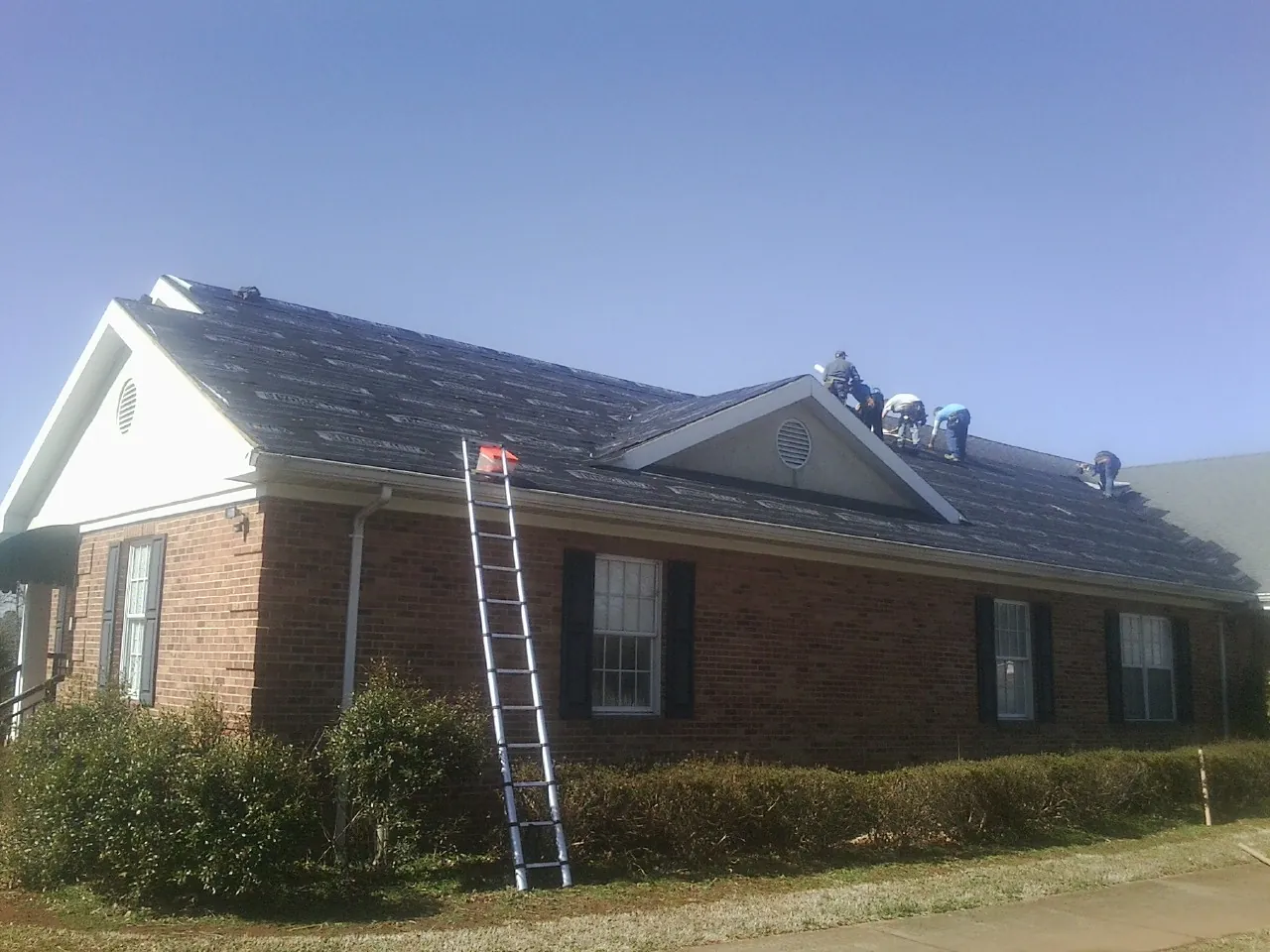 Crew tearing shingles off a brick ranch roof with a ladder set — Emergency Roof Repair work by our crew in Sublimity