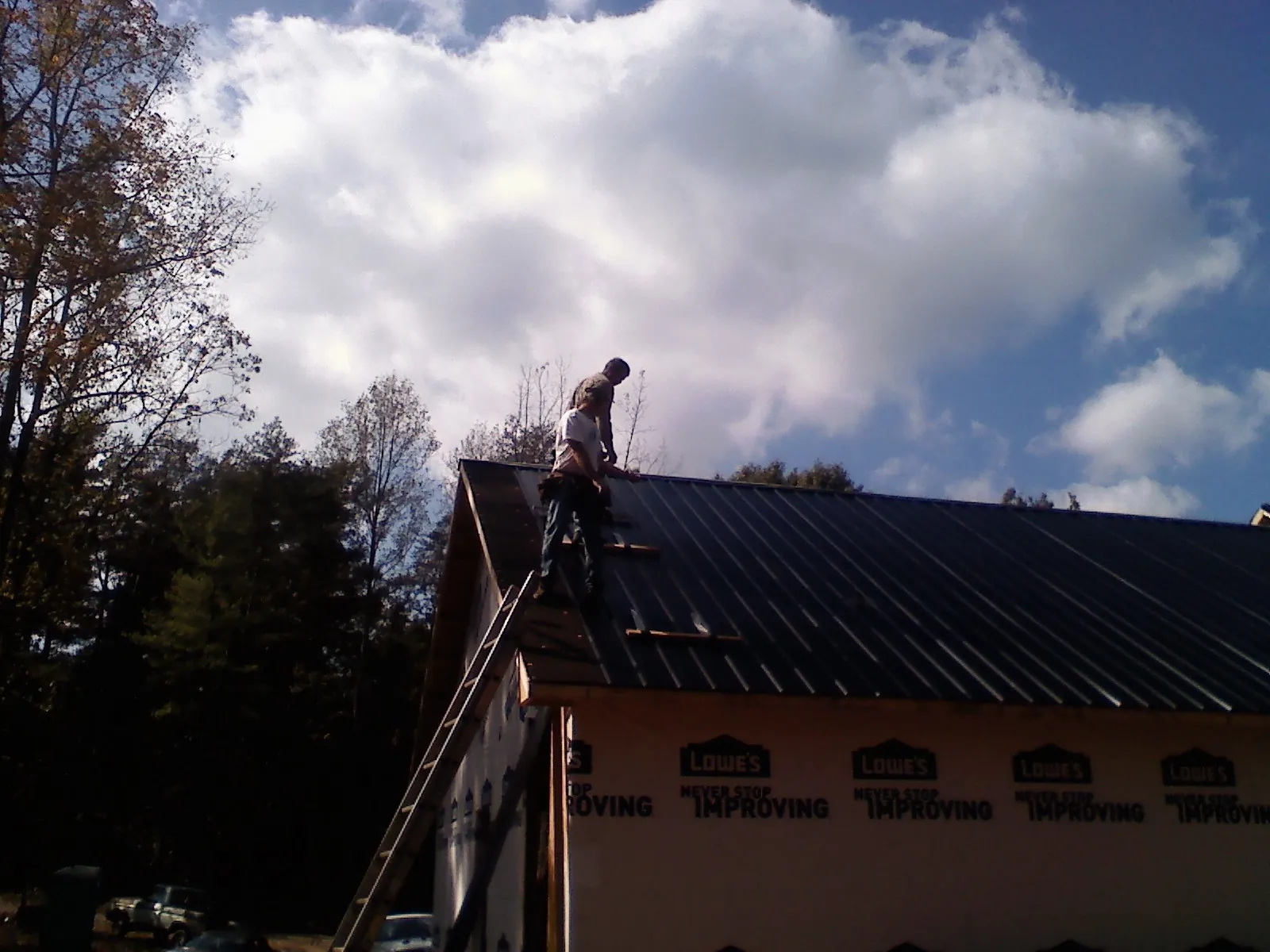 Roofer fastening dark metal panels high against a cloudy sky, from a Roof Inspection job in Sublimity